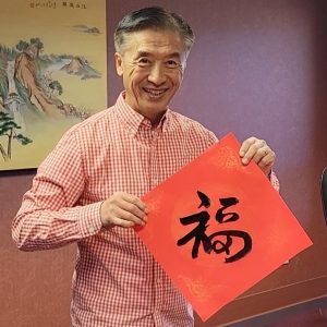 CCAI co-Founder and President Joshua Zhong is holding up a red Chinese blessing page with a fresh-painted calligraphy Blessing character by his truly.